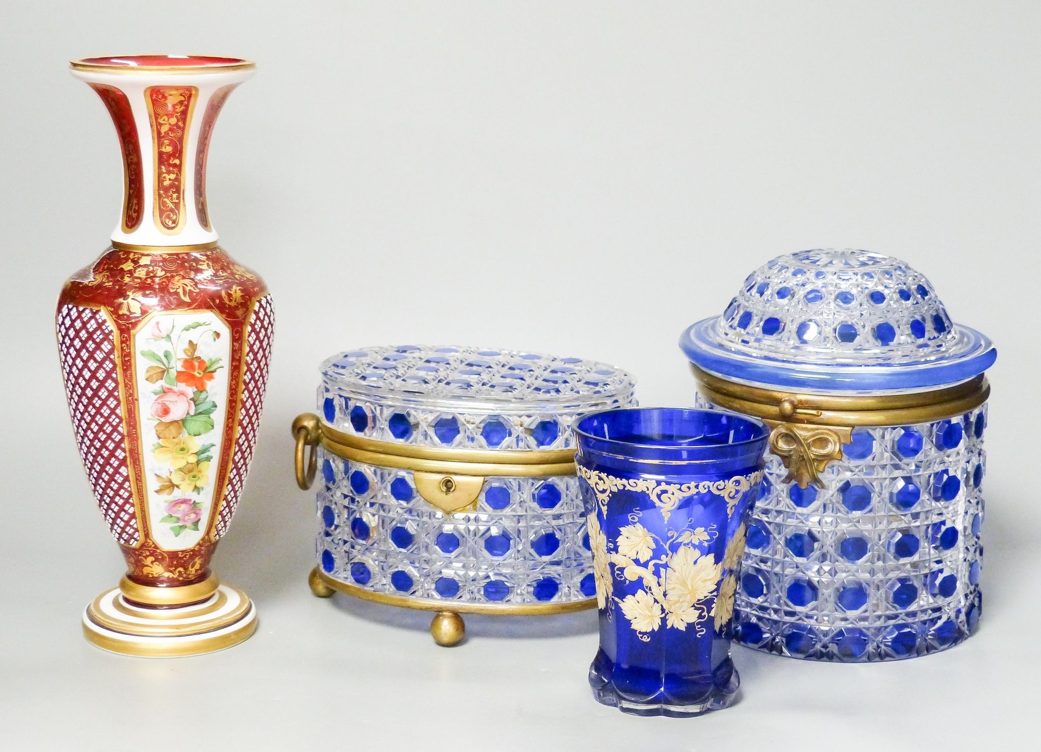 A 19th century Bohemian overlaid glass vase, 25.5cm, a similar gilded and enamelled beaker and two blue flashed hobnail glass biscuit boxes and covers